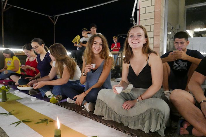 Las mujeres jóvenes están sentadas en una azotea por la noche con una vela encendida frente a ellas.