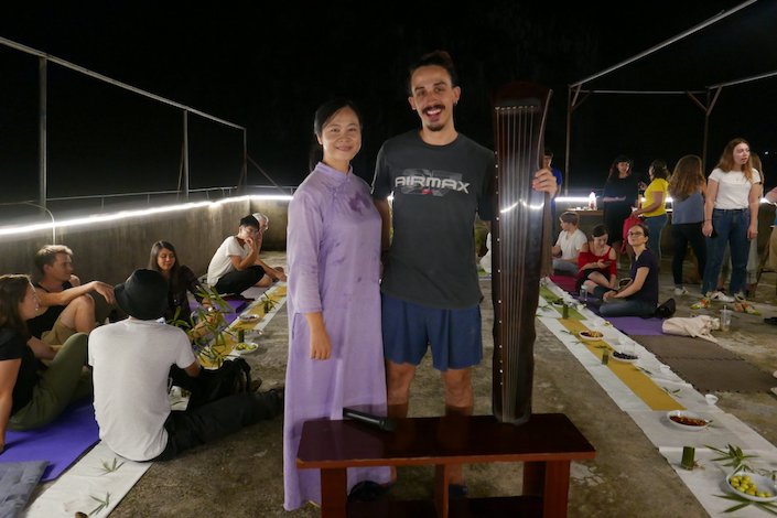 一位身穿紫色衣服的年轻女士和一位手持中国古筝的年轻人晚上站在屋顶上