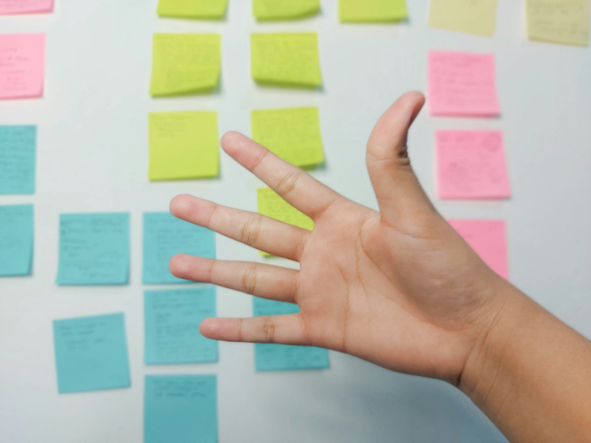 A hand against a background of a whiteboard with post it notes
