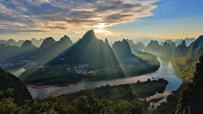 karst mountains in yangshuo with the sunrise behind them breaking through the clouds