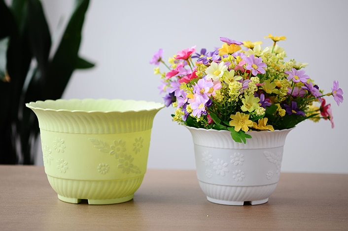 a pot full of fake flowers sits next to an empty plastic flower pot