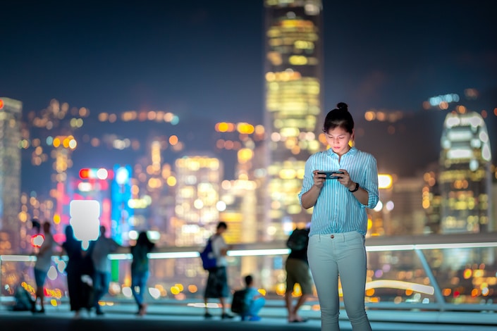 Mujer con smartphone en la noche con Victoria Horbor en segundo plano.