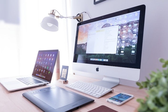 un ordinateur de bureau de marque Apple assis sur un bureau avec un ordinateur portable et un téléphone portable de chaque côté
