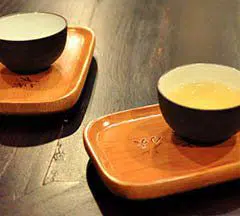 Two tea cups on wooden trays on a dark tabletop