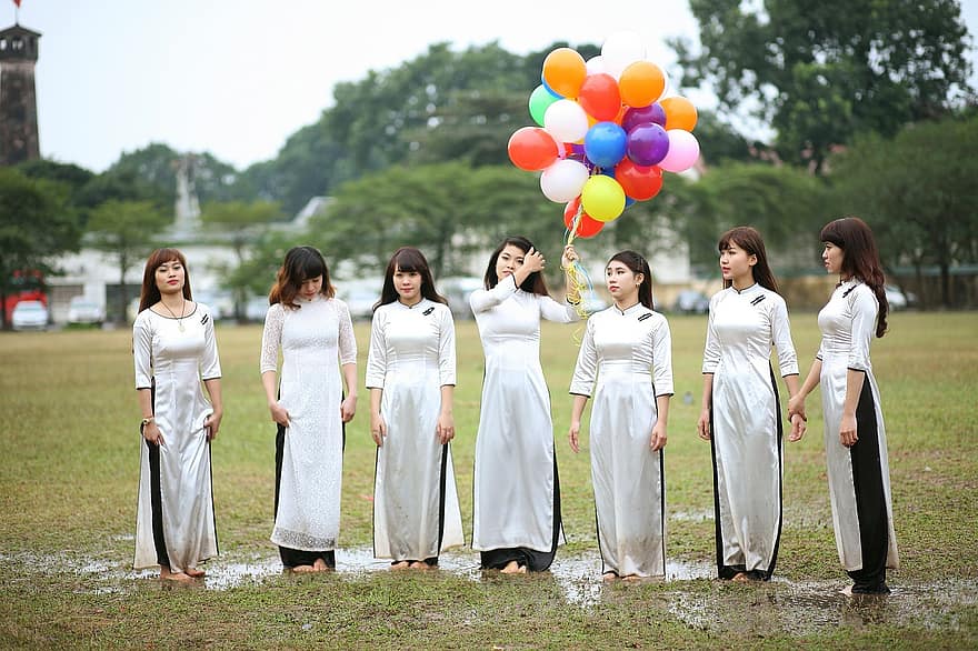 una foto de mujeres chinas jóvenes vestidas de blanco, con la del centro sosteniendo globos de colores para decir feliz cumpleaños en chino