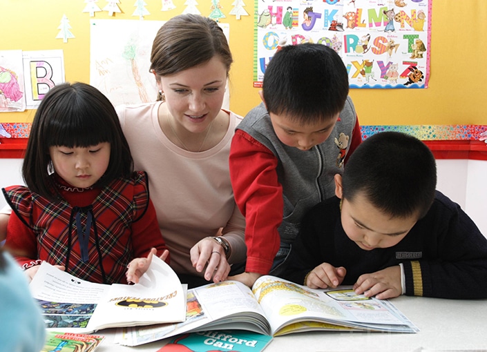 a western woman looks at a book with three young Chinese students