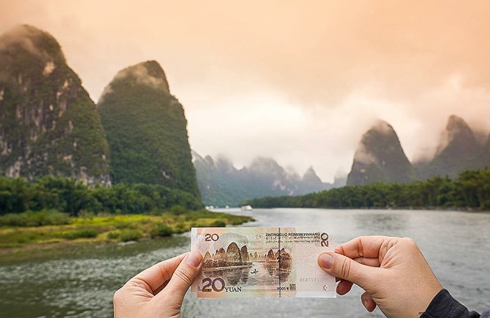 a Chinese 20RMB note being held up against the scenic background depicted on it