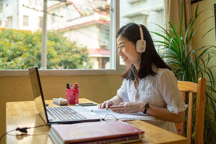 un profesor de CLI sentado en un escritorio ayudando a un estudiante a aprender chino en Zoom