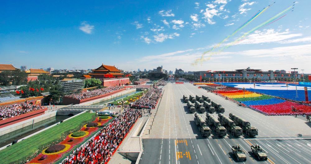 crowds watch a colorful Chinese National Day Parade on Tian'anmen Square under a blue sky as planes fly overhead