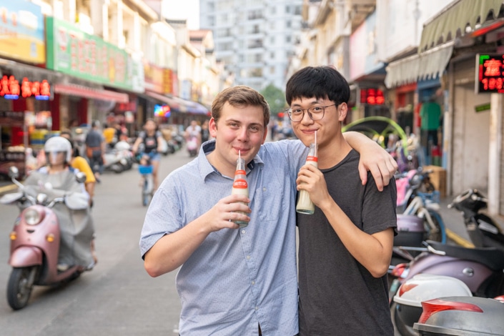a Chinese and western man drinking a beverage with their arms around each other