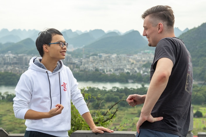 a Chinese and western man talking with mountains in the background