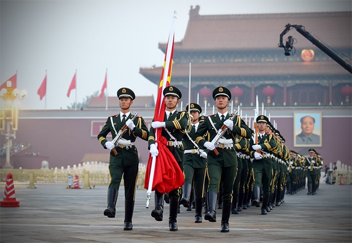 Chinese soldiers, one of whom carries a Chinese flag, march in formation outside the Forbidden City in Beijing, China on Chinese National Day