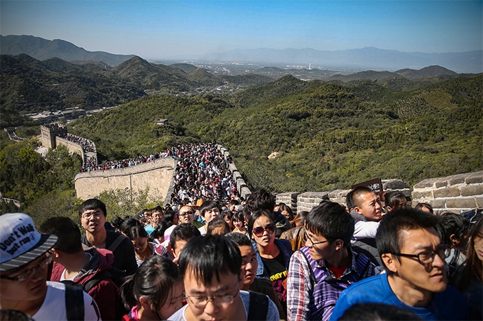 a crowd of tourists walks on the Great Wall of China with mountains in the background on Chinese National Day