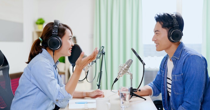 a Chinese man and woman wearing headphones talking to each other while recording a Chinese podcast