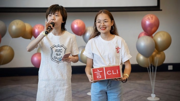 deux membres du personnel de CLI se tiennent debout avec des ballons en arrière-plan tout en organisant une tombola lors d'un événement d'anniversaire de CLI