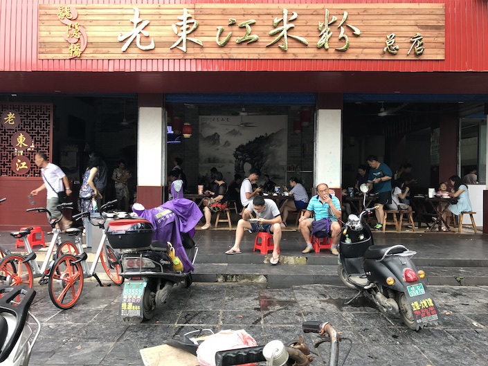 gente sentada en los escalones y dentro de Laodongjiang, un restaurante mifen en Guilin