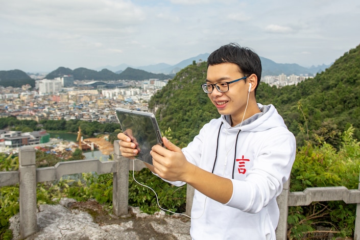 a CLI teacher teaches a student Chinese over Zoom while standing on a mountaintop