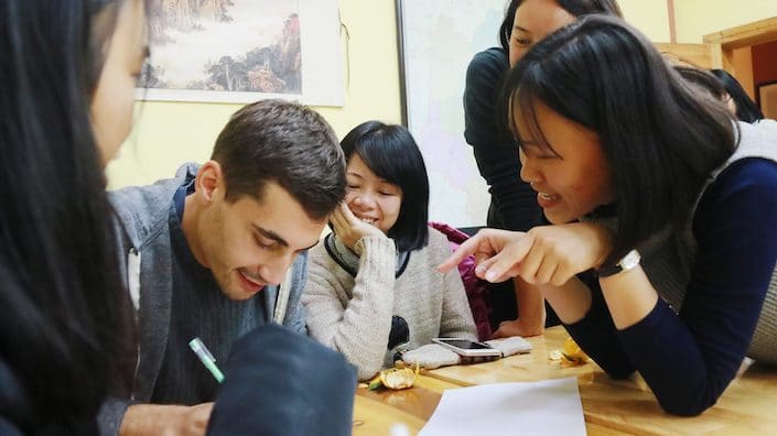 a CLI student practices writing Chinese characters as several CLI teachers look on