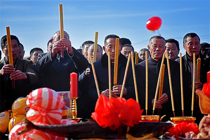 a group of Chinese men burn incense to honor deceased family members