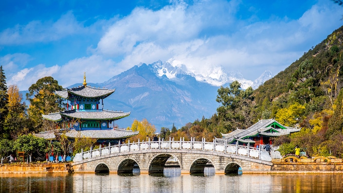 a landscape showing a temple, a bridge over a lake and a snowcapped mountain in the background