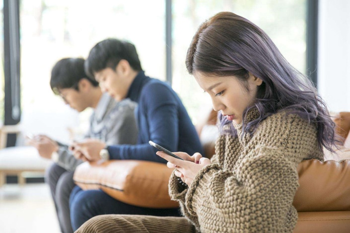 una mujer china mirando un teléfono inteligente mientras dos hombres chinos hacen lo mismo en el fondo