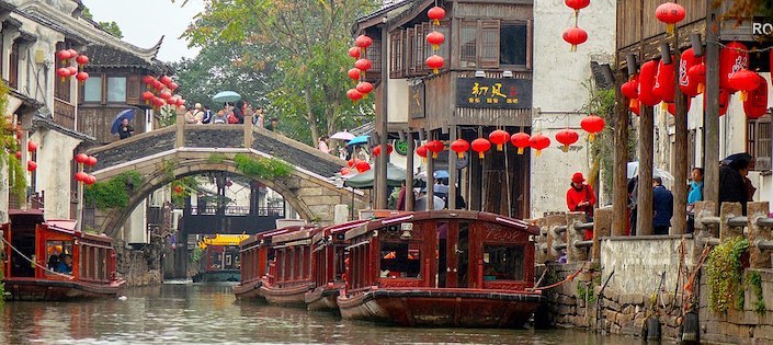 a Suzhou travel guide directs tourists near a canal with traditional houses and red lanterns in the background in Suzhou, China