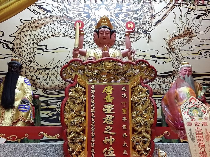 a Chinese deity on an alter with a drawing of a dragon on the wall behind it