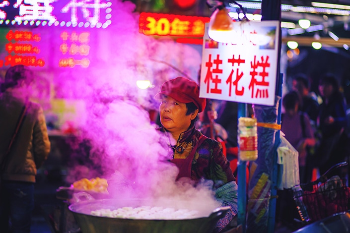 中国街头小贩端着一锅热气腾腾的食物