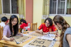 Students practice brush calligraphy with a teacher at a long table