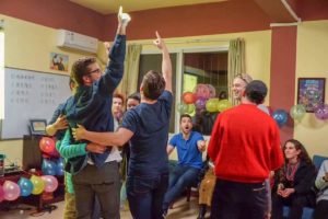 People cheer and point upward at a party with colorful balloons