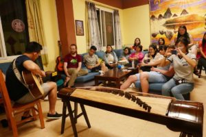 A man plays guitar beside a guzheng as a group listens in the lounge