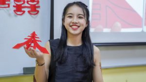 A smiling woman holds up a red Chinese paper cutting