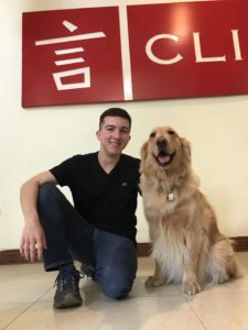 A man kneels beside a golden retriever under the red CLI sign