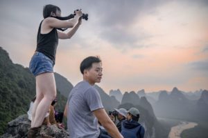 A woman photographs karst peaks at dusk while a man sits on the rocks