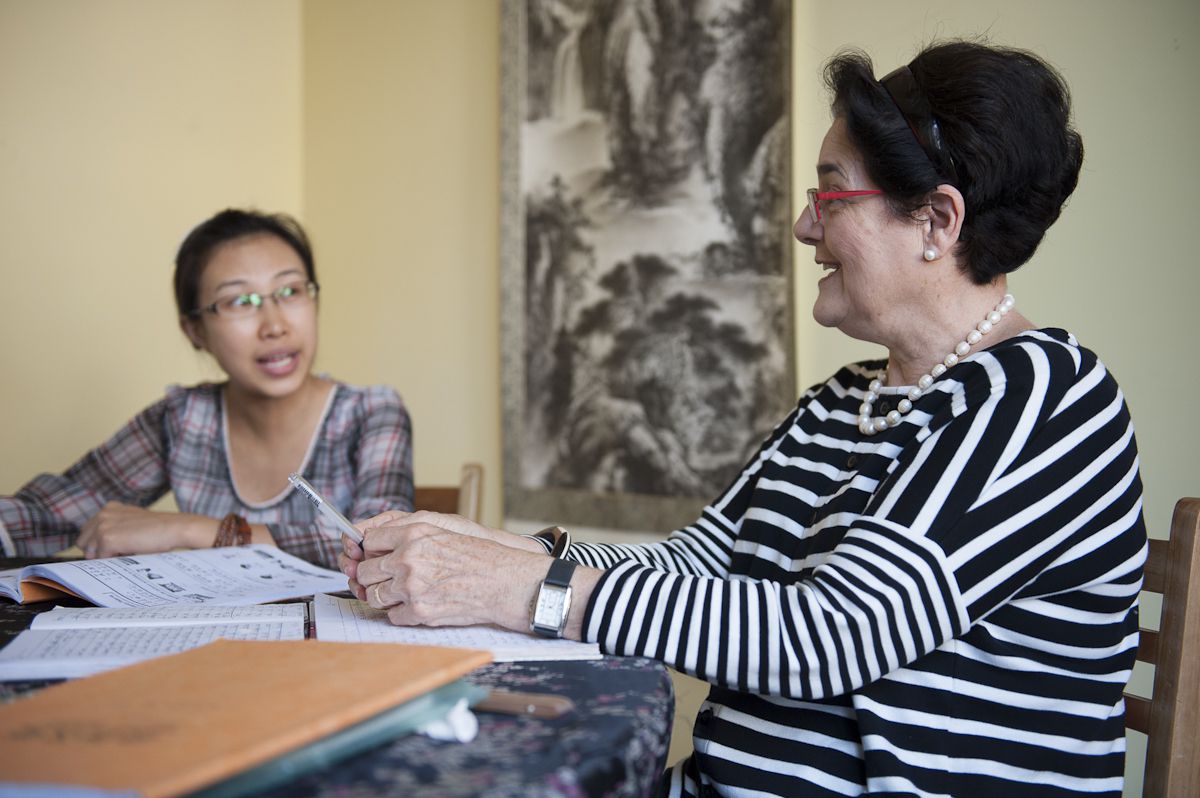 una mujer occidental mayor se sienta en una mesa y habla con su maestra de chino durante la clase en CLI