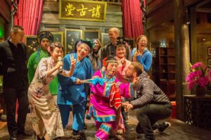 A group poses with costumed folk opera performers in a decorated hall