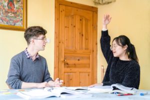 A teacher raises her hand while a student listens across the table