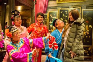 A woman in a green coat laughs with performers in colorful costumes