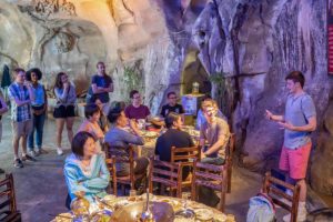 A group gathers around tables inside a large limestone cave