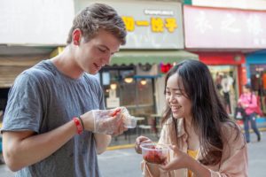 Two people laugh while trying street food from small cups