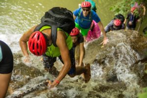 Hikers in helmets climb up through a rushing waterfall