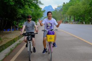 Two people ride bicycles along a quiet road among karst hills