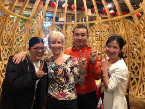 Four friends pose inside a lantern-lit decorative wooden pavilion
