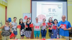 Students hold up their red paper cuttings after a workshop