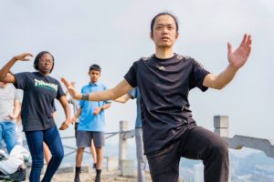 A man leads a tai chi move on a hilltop as others follow behind