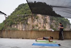 A woman holds a plank on a rooftop mat below a karst cliff