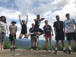 A group poses on a hilltop lookout as two people jump in the air