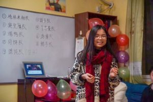 A smiling woman in a red scarf stands by a whiteboard and balloons