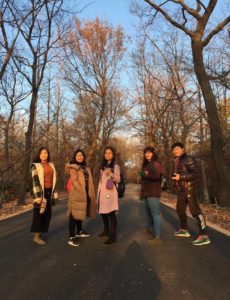 Five people stand on a road lined with bare autumn trees