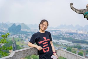 A woman in a CLI T-shirt leans on a railing above Guilin